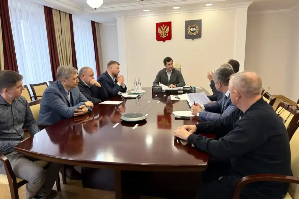 Участники рабочей встречи сидят за длинным столом с документами.