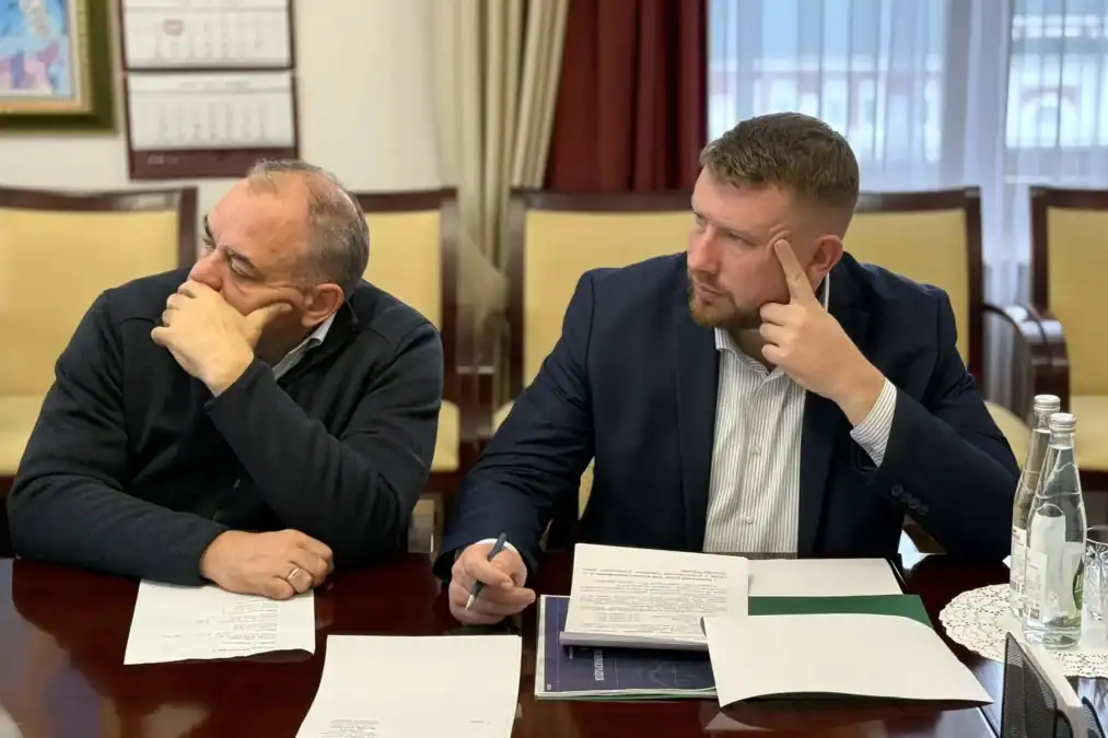 Двое мужчин изучают документы и делают записи за столом.