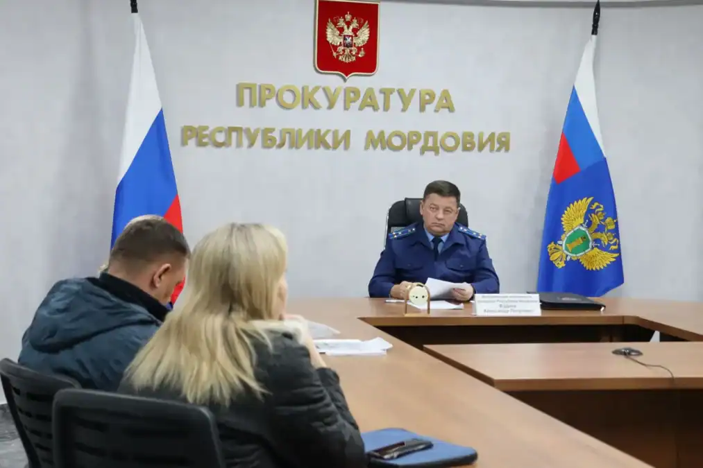 Прокурор в синем мундире беседует с двумя посетителями за столом.