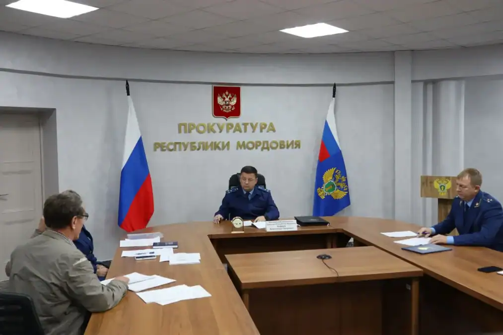 Сотрудники прокуратуры и посетители сидят за столами с документами.