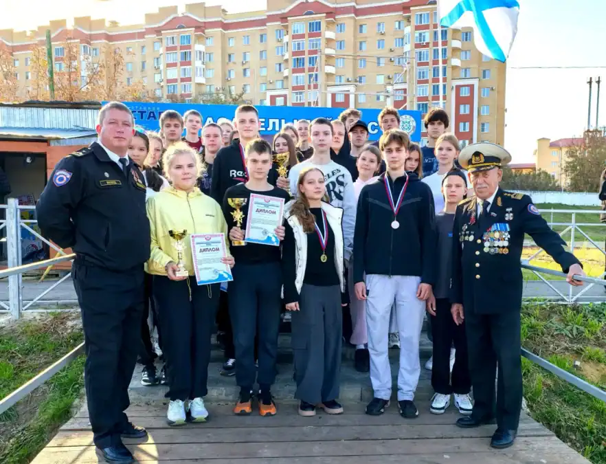 Школьники с грамотами и медалями стоят рядом с двумя мужчинами в форме.