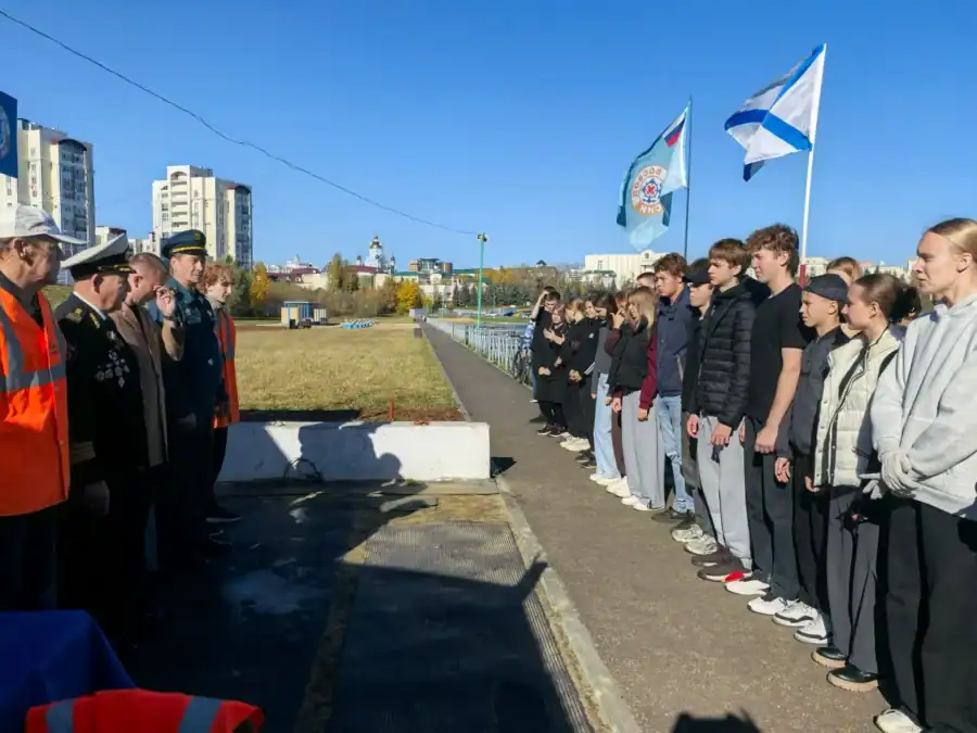 Школьники выстроились напротив представителей спасательных служб у берега водоёма.
