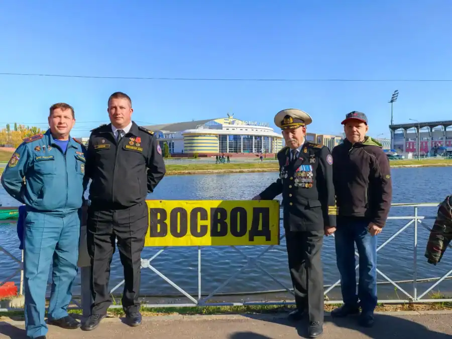 Четверо мужчин стоят у берега рядом с вывеской «ВОСВОД».