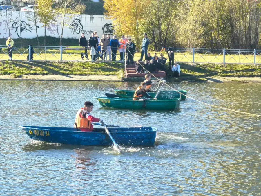 Два участника в спасательных жилетах гребут на лодках по водоёму.