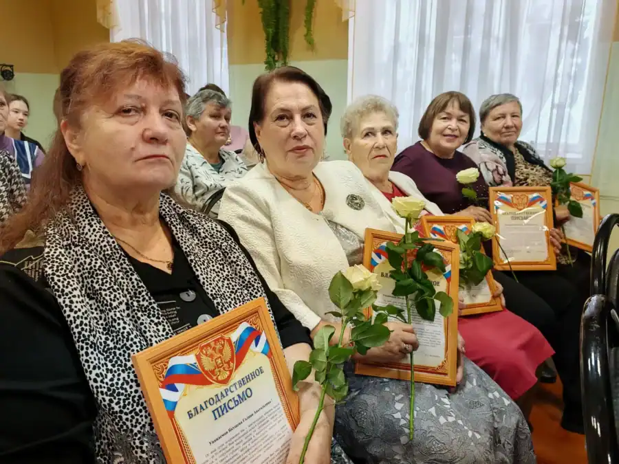 Женщины в зале сидят с благодарственными письмами и букетами белых роз.
