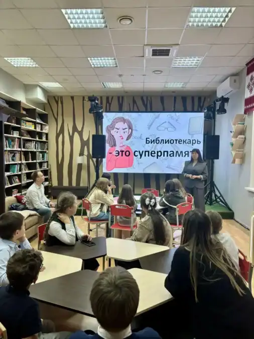 Дети слушают выступление сотрудницы перед экраном в библиотечном центре.