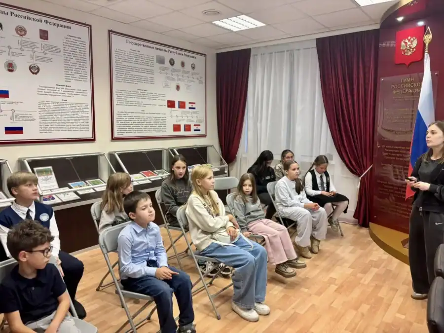 Дети слушают экскурсовода в зале с государственными символами.