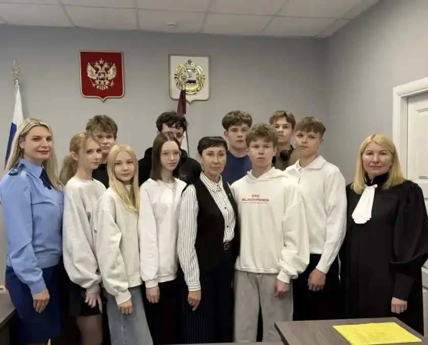 Школьники и две сотрудницы позируют в помещении с государственными гербами на стене.