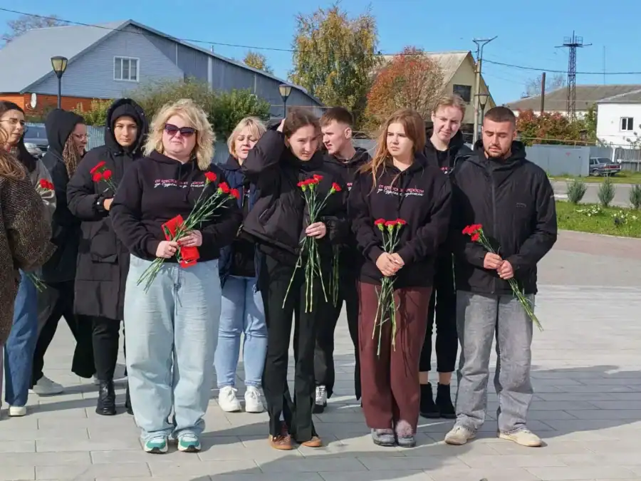 Группа молодых людей держит красные гвоздики на мемориальной площади.
