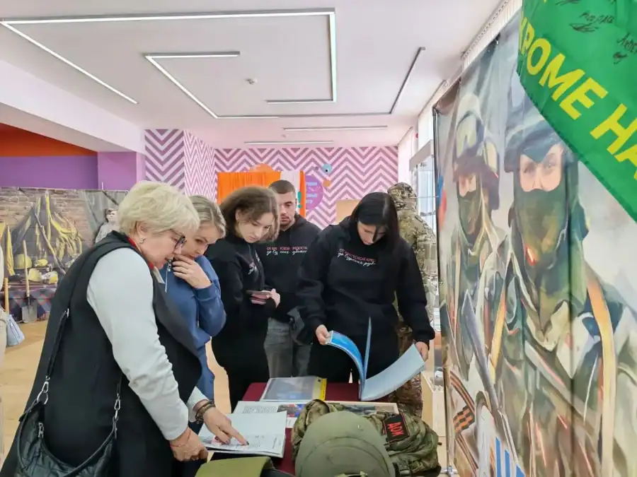 Посетители рассматривают книги и военные предметы на музейной выставке.