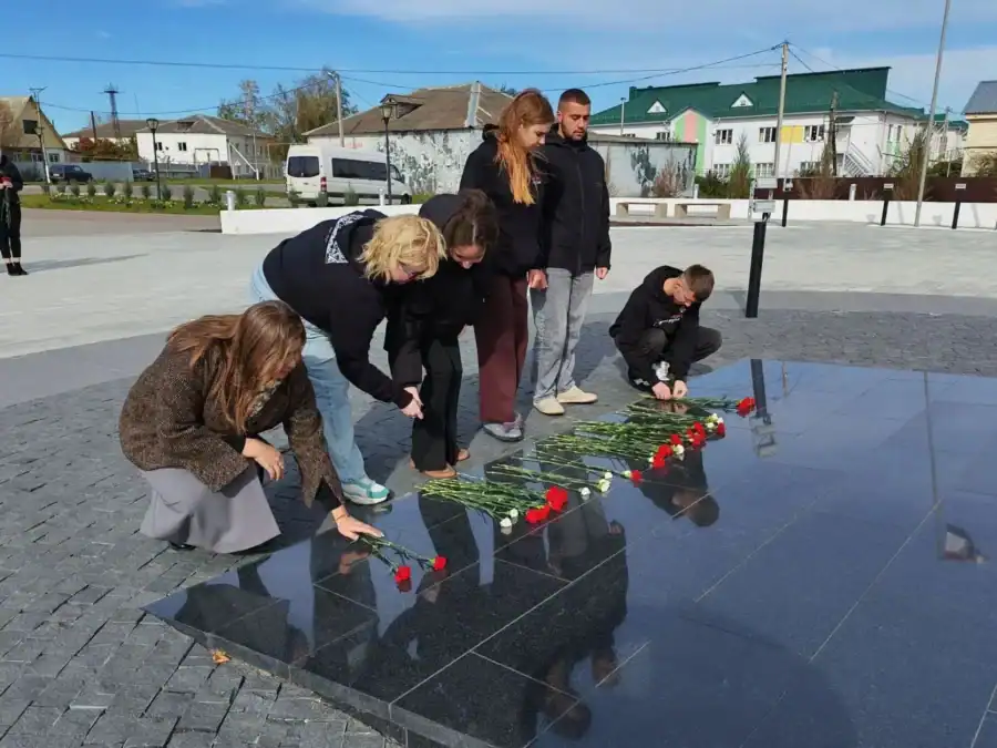 Участники возлагают красные гвоздики к чёрному гранитному мемориалу.