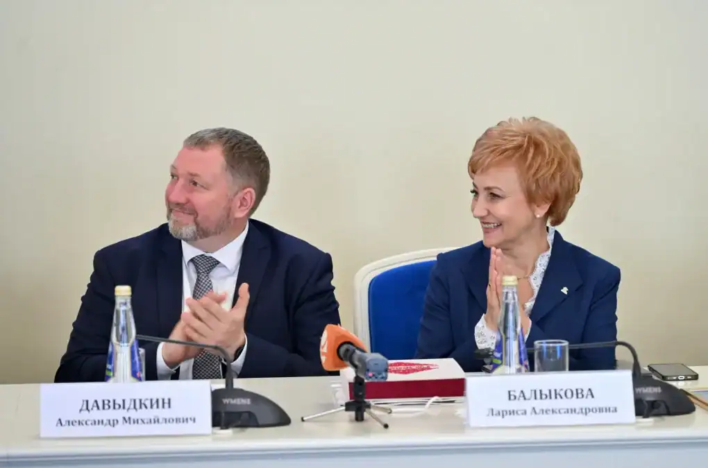 Двое участников панели сидят за столом с именными табличками и микрофонами.