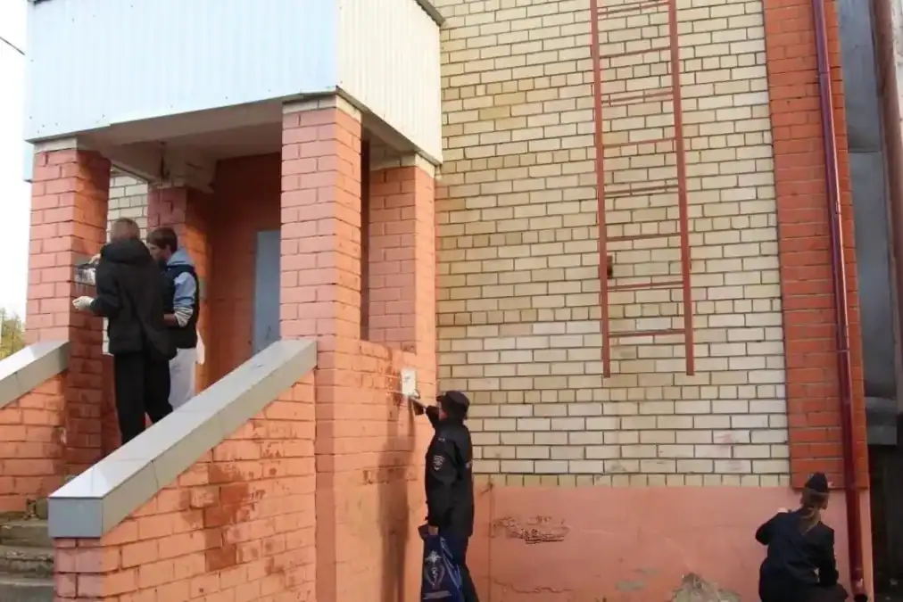 Сотрудники полиции и другие участники закрашивают надписи у подъезда кирпичного дома.