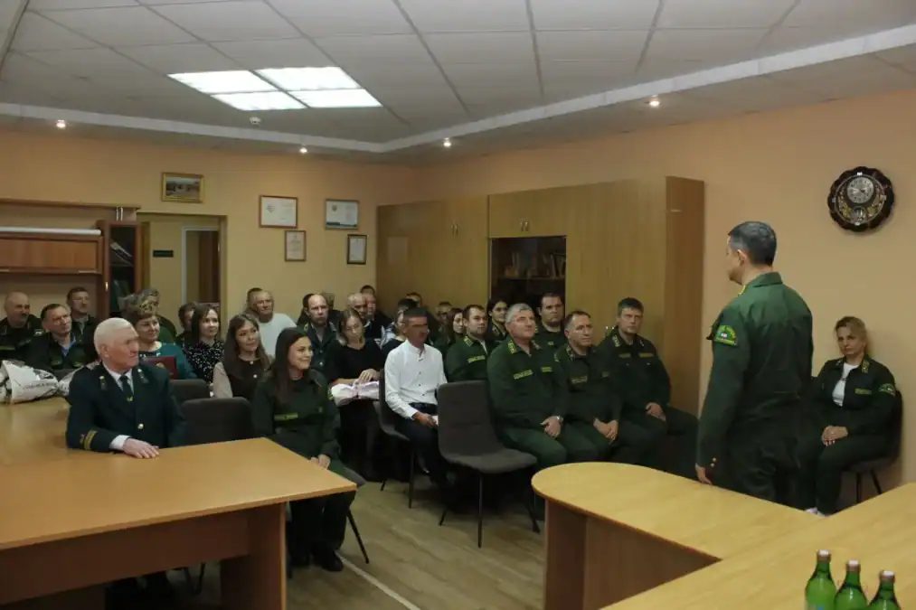 Сотрудники лесной службы сидят в кабинете и слушают выступающего коллегу в форме.