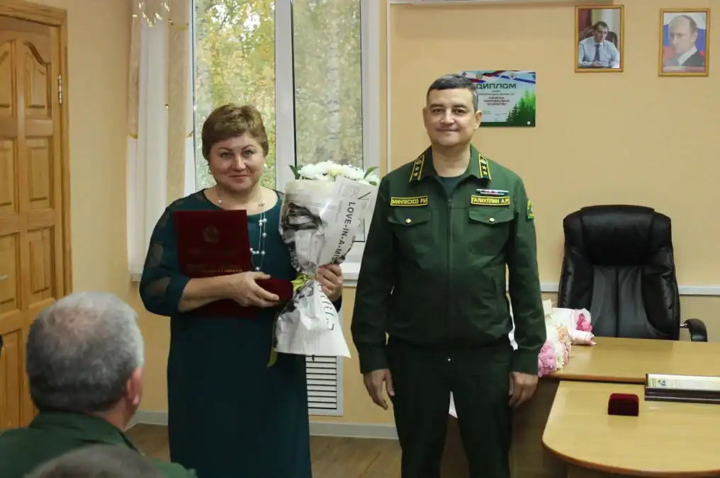 Женщина с букетом и наградным футляром стоит рядом с сотрудником лесной службы.
