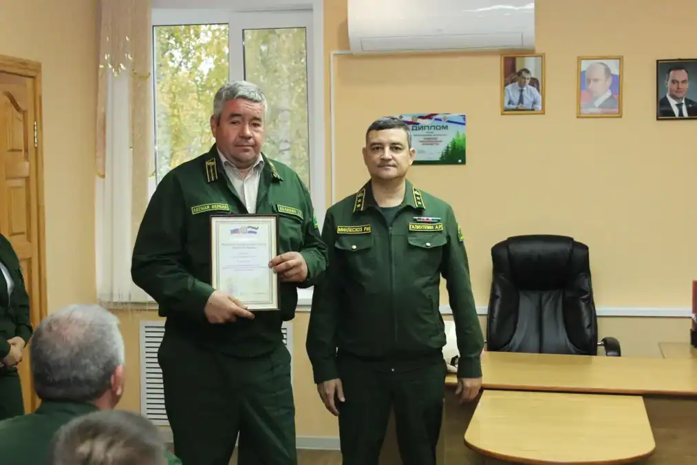 Мужчина показывает оформленную благодарность рядом с сотрудником лесной службы.