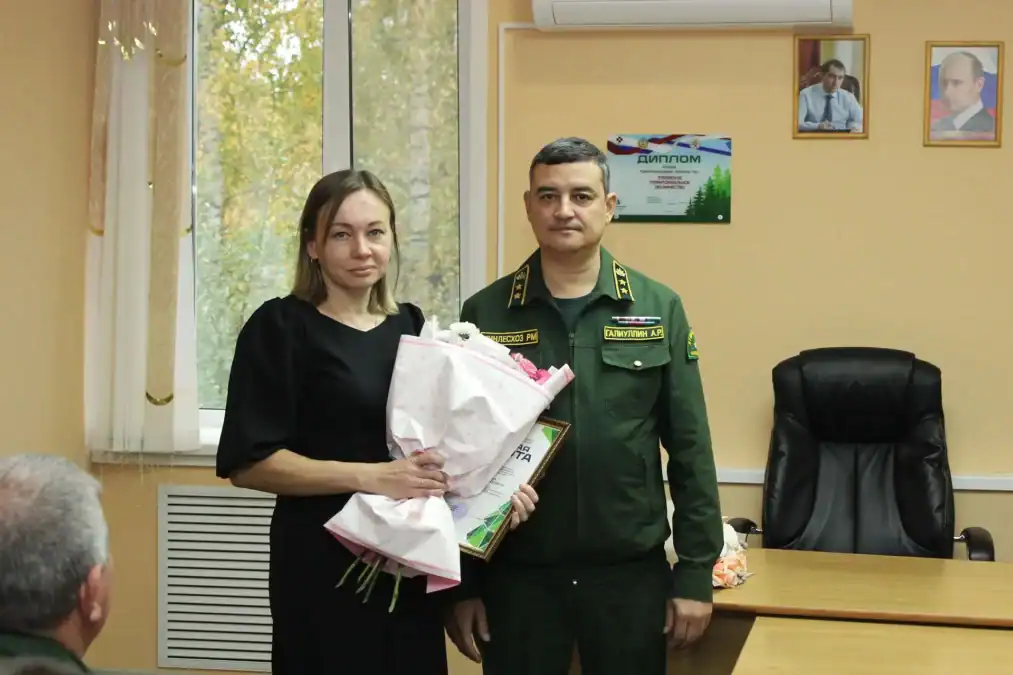 Женщина с букетом и грамотой стоит рядом с сотрудником лесной службы.