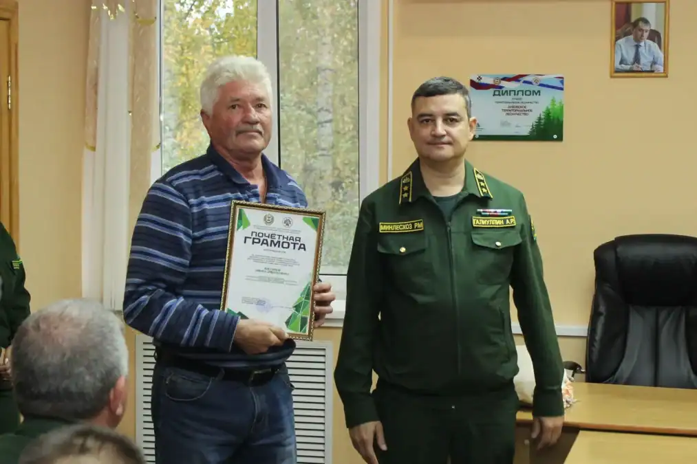 Мужчина держит почётную грамоту рядом с сотрудником лесной службы.