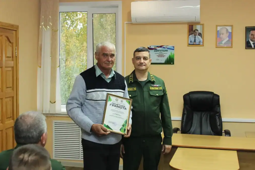 Мужчина показывает почётную грамоту рядом с сотрудником лесной службы.