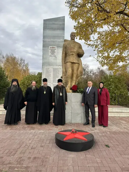 Священнослужители и представители администрации стоят у памятника воину с красной звездой.