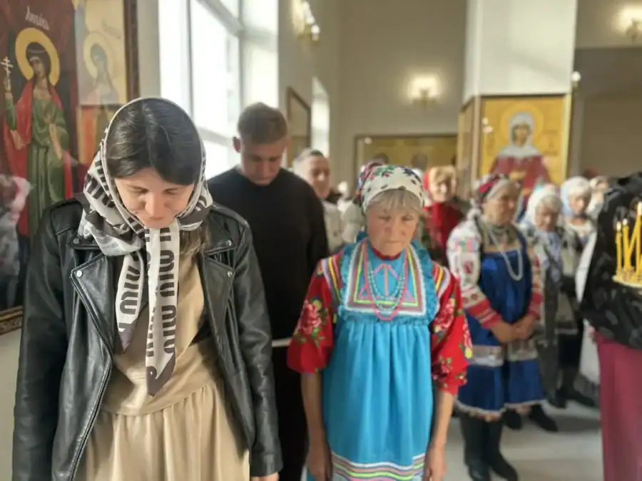 Женщины в платках и народных костюмах стоят в храме во время службы.
