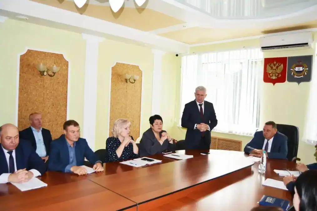Мужчина выступает перед сидящими за столом участниками заседания.