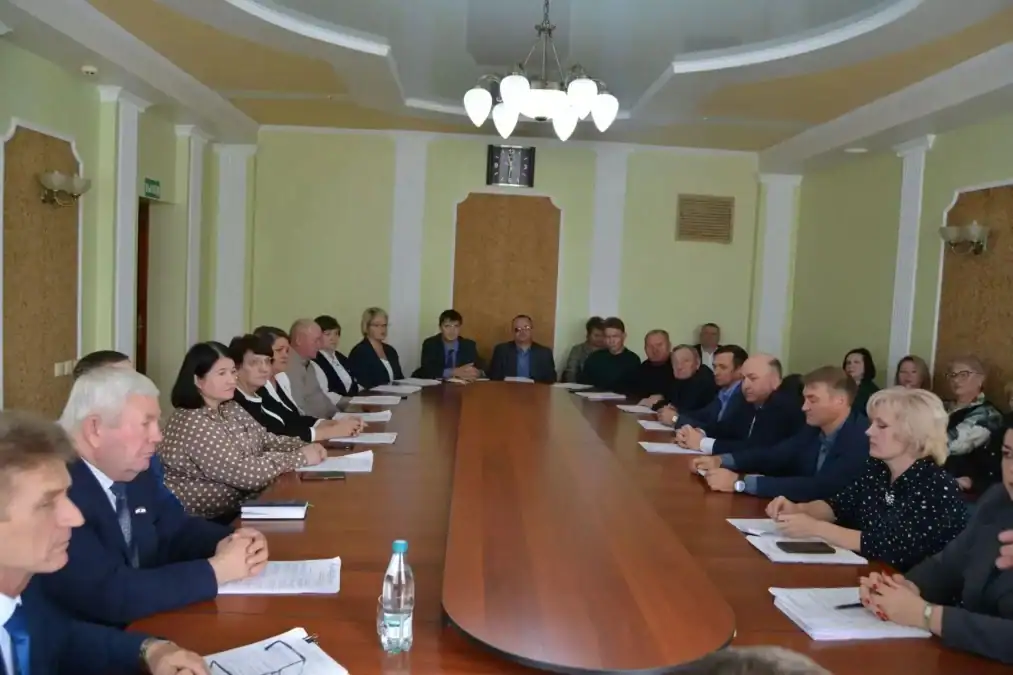 Участники совещания сидят по обеим сторонам длинного стола с документами.