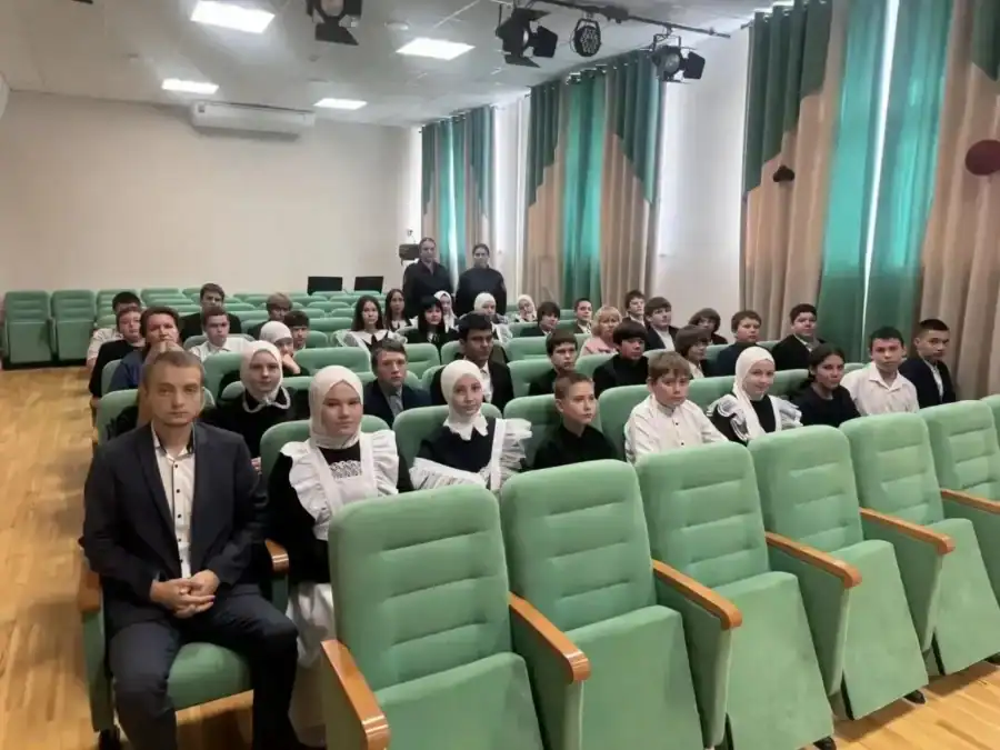 Школьники и взрослые сидят в зрительном зале перед мероприятием.