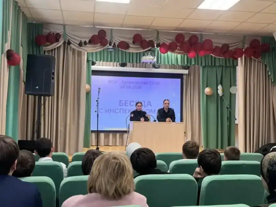 Сотрудники выступают со сцены перед школьниками в актовом зале.