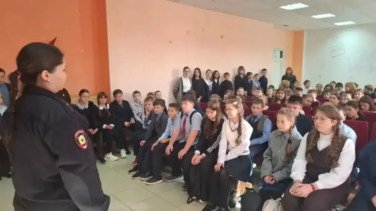Сотрудница полиции в форме беседует с большой группой школьников.