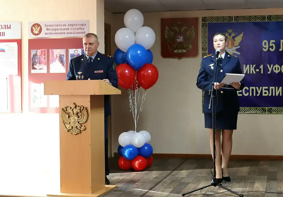 Сотрудники в форме выступают у трибуны и микрофона в украшенном зале.