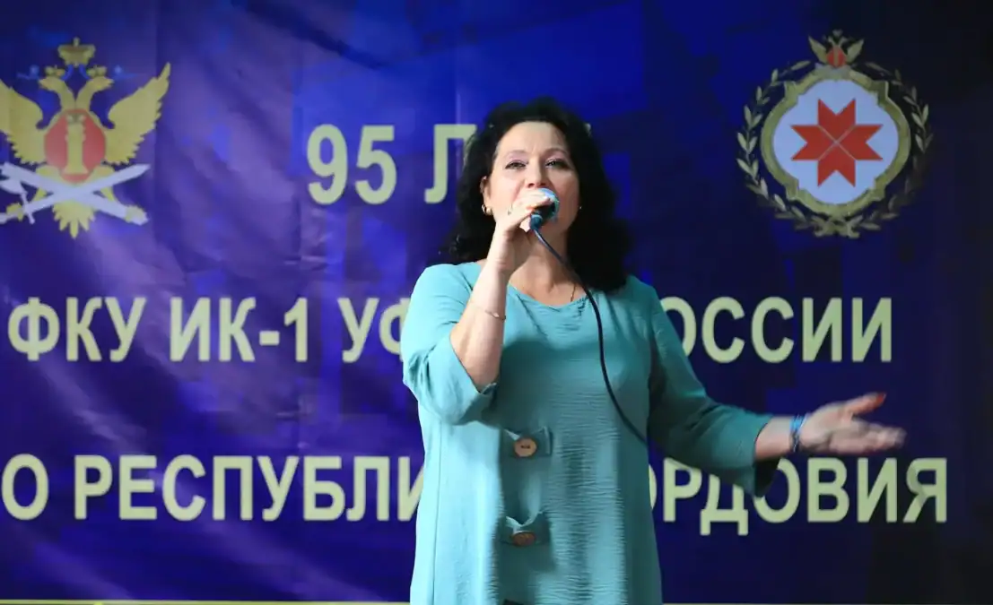 Женщина в бирюзовом платье исполняет песню у микрофона.