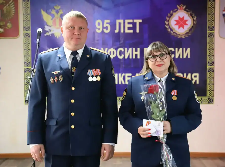 Сотрудница в форме с букетом стоит рядом с мужчиной в парадной форме.