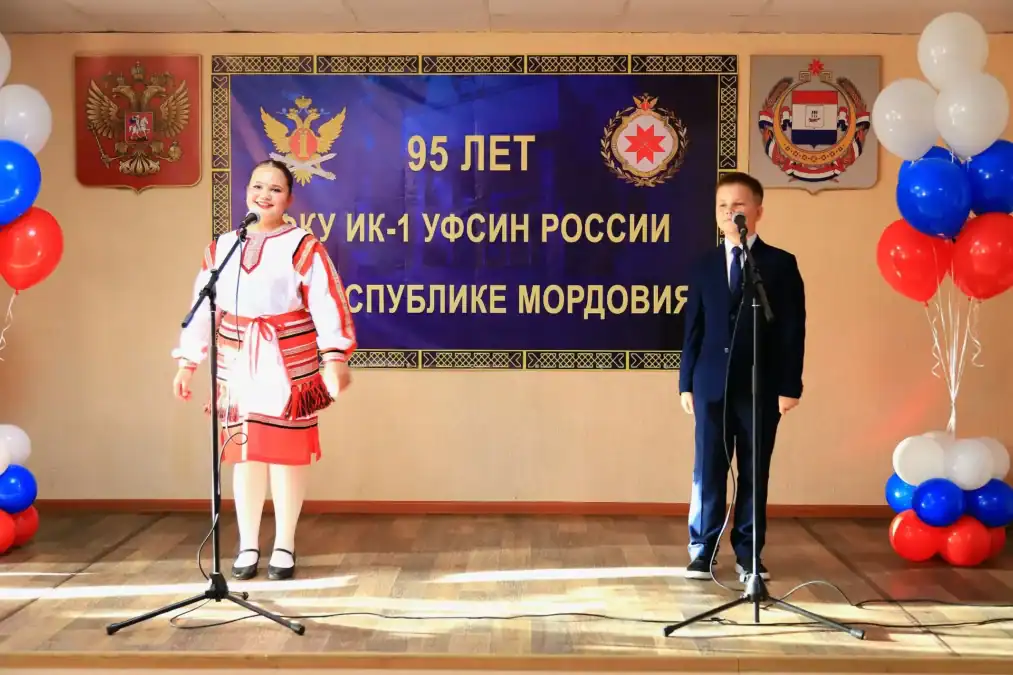 Мужчина и женщина выступают у микрофонов перед юбилейным баннером.