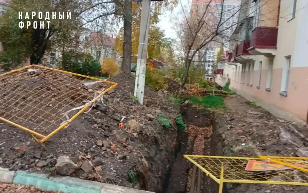 Глубокая траншея и ограждения во дворе многоквартирного дома.