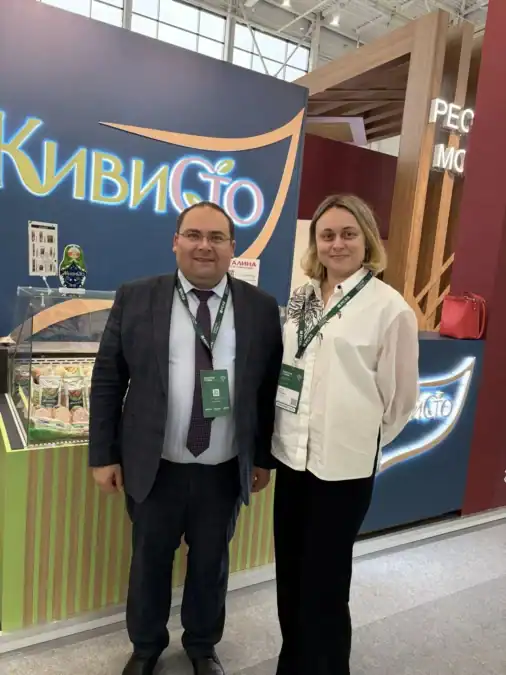 Двое участников с бейджами стоят у стенда с продукцией «КивиСто».