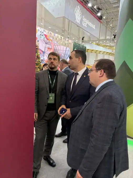 Трое мужчин с бейджами осматривают экспозицию на выставке.