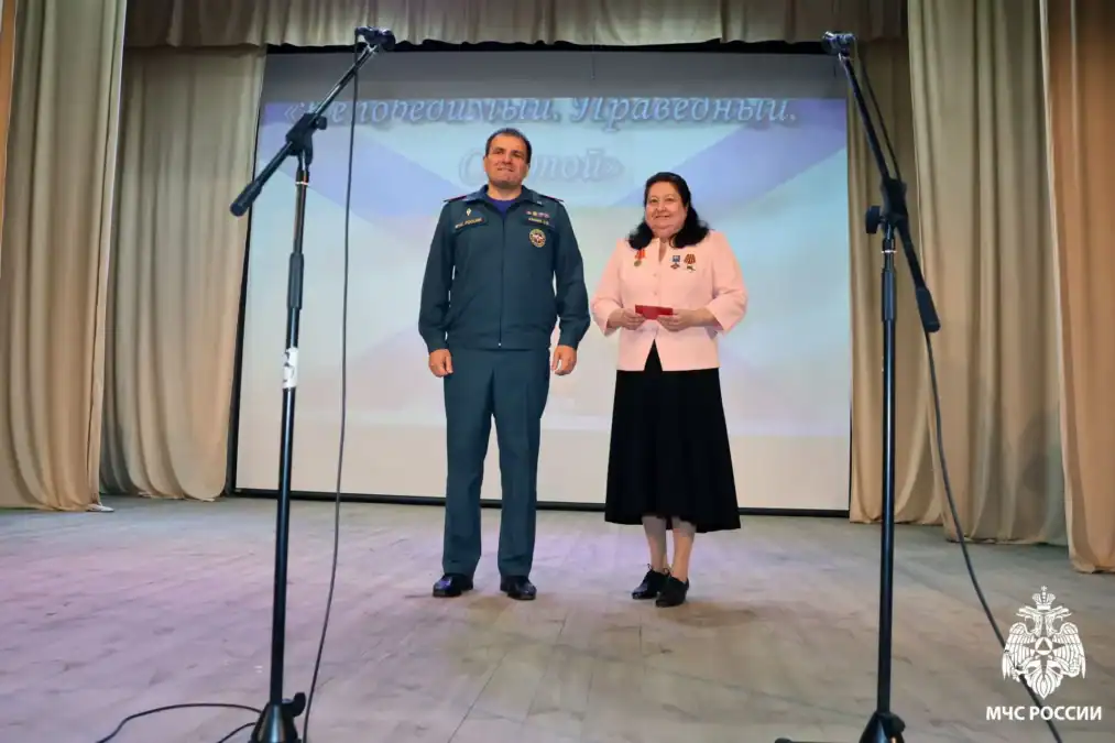 Мужчина в форме МЧС и женщина стоят на сцене между микрофонами.
