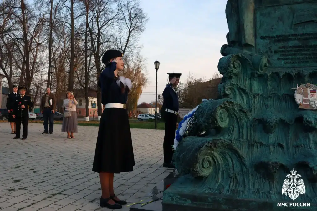 Девушка в морской форме отдаёт честь у подножия памятника с венком.
