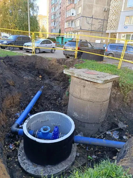 Открытый водопроводный колодец с синими трубами на участке земляных работ.