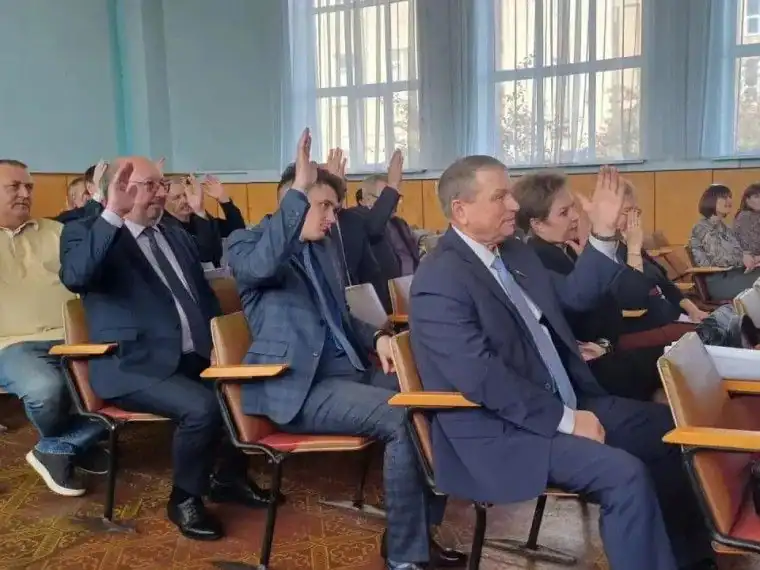 Участники заседания сидят в зале и поднимают руки для голосования.