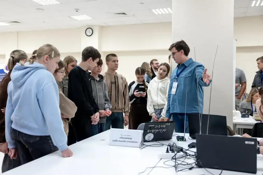 Наставник показывает группе школьников оборудование и ноутбук на техническом мастер-классе.