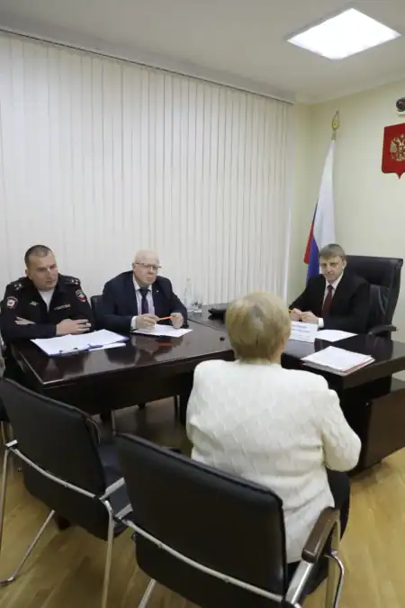 Министр, сотрудник полиции и посетительница сидят за столом с документами.