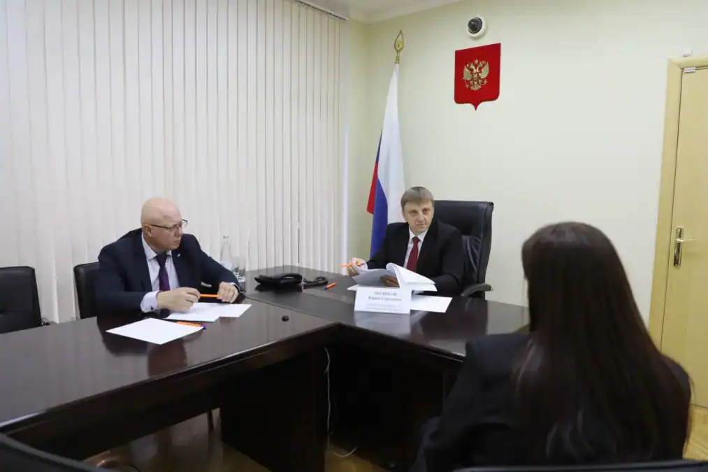 Мужчина за рабочим столом просматривает документы в присутствии посетительницы.