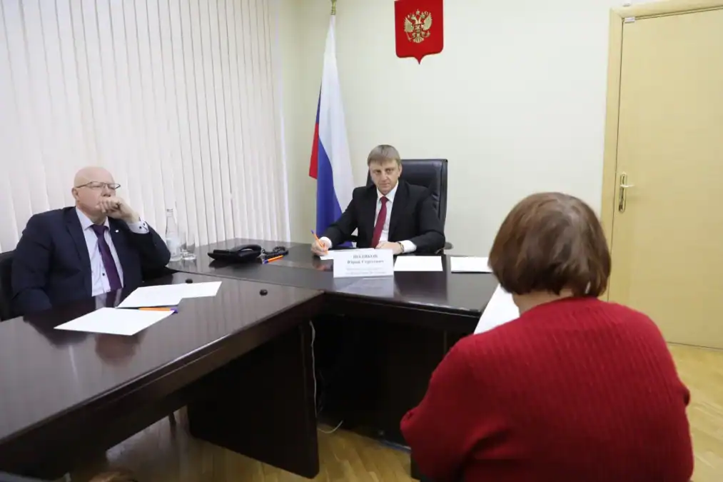 Мужчины за столом беседуют с посетительницей в кабинете.