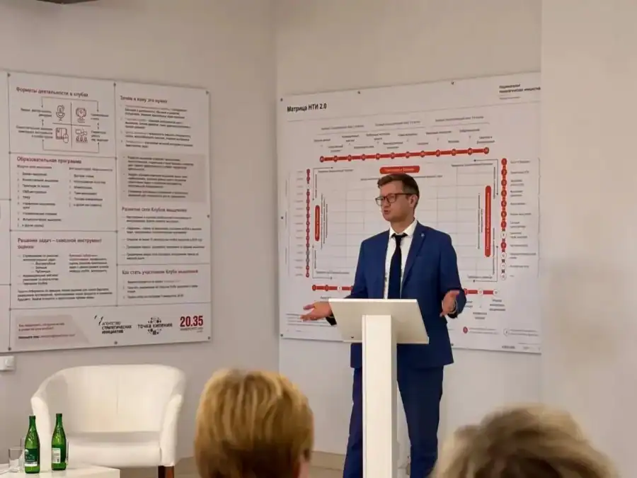 Мужчина в синем костюме выступает за кафедрой перед слушателями.