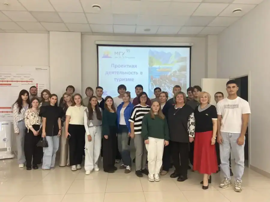 Студенты и преподаватели позируют перед экраном с презентацией о туризме.