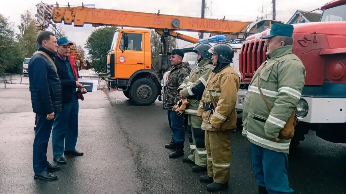 Сотрудники экстренных служб стоят у пожарной машины и автокрана.