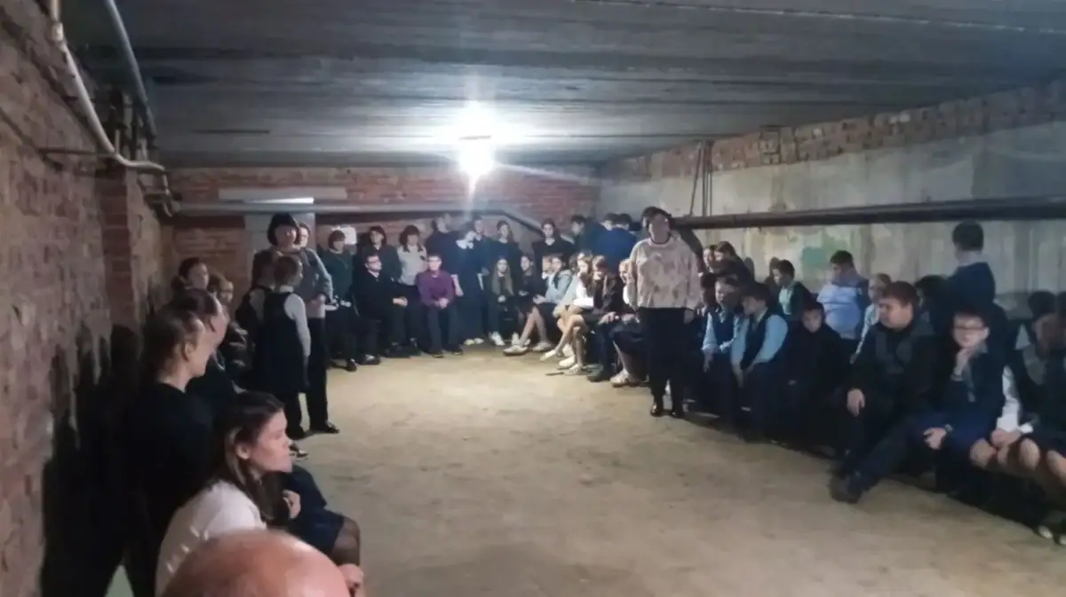 Группа школьников и взрослых находится в подвальном помещении с кирпичными стенами.