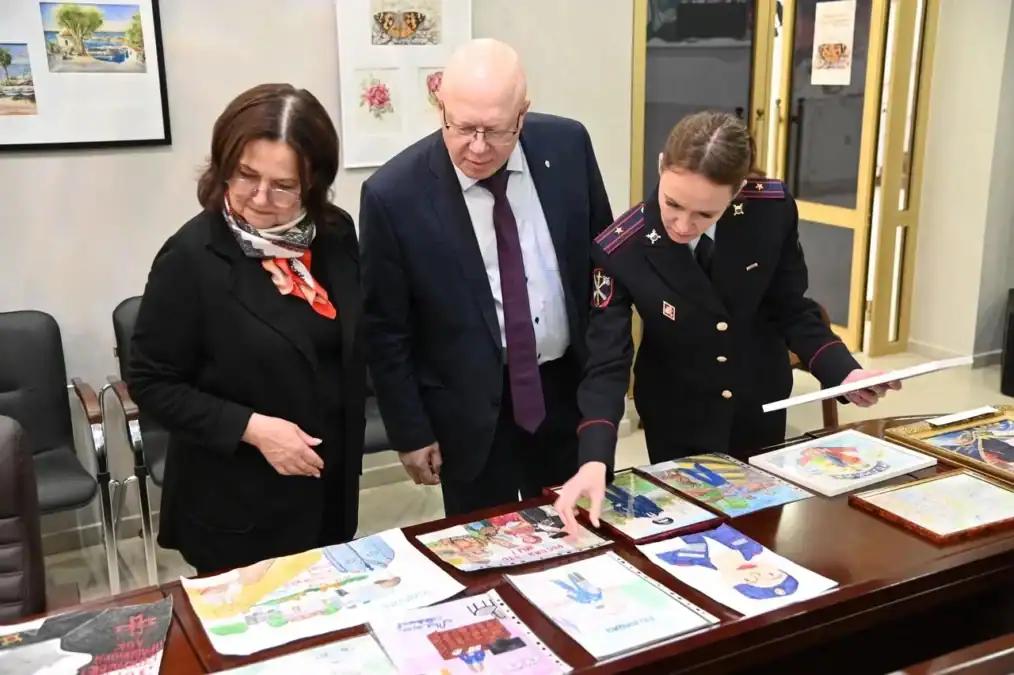 Трое членов жюри изучают разложенные на столе конкурсные рисунки.